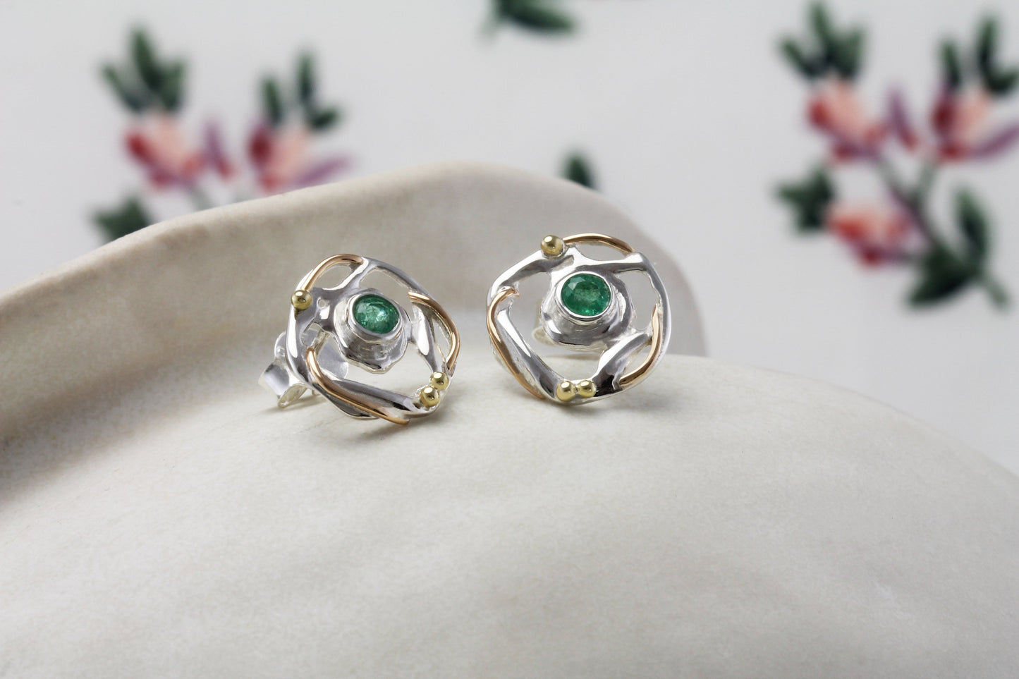 Pair of silver and gold earrings with green gemstones on a white surface.
