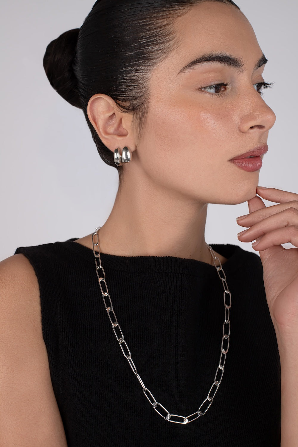 Woman wearing a silver chain necklace and earrings against a plain background