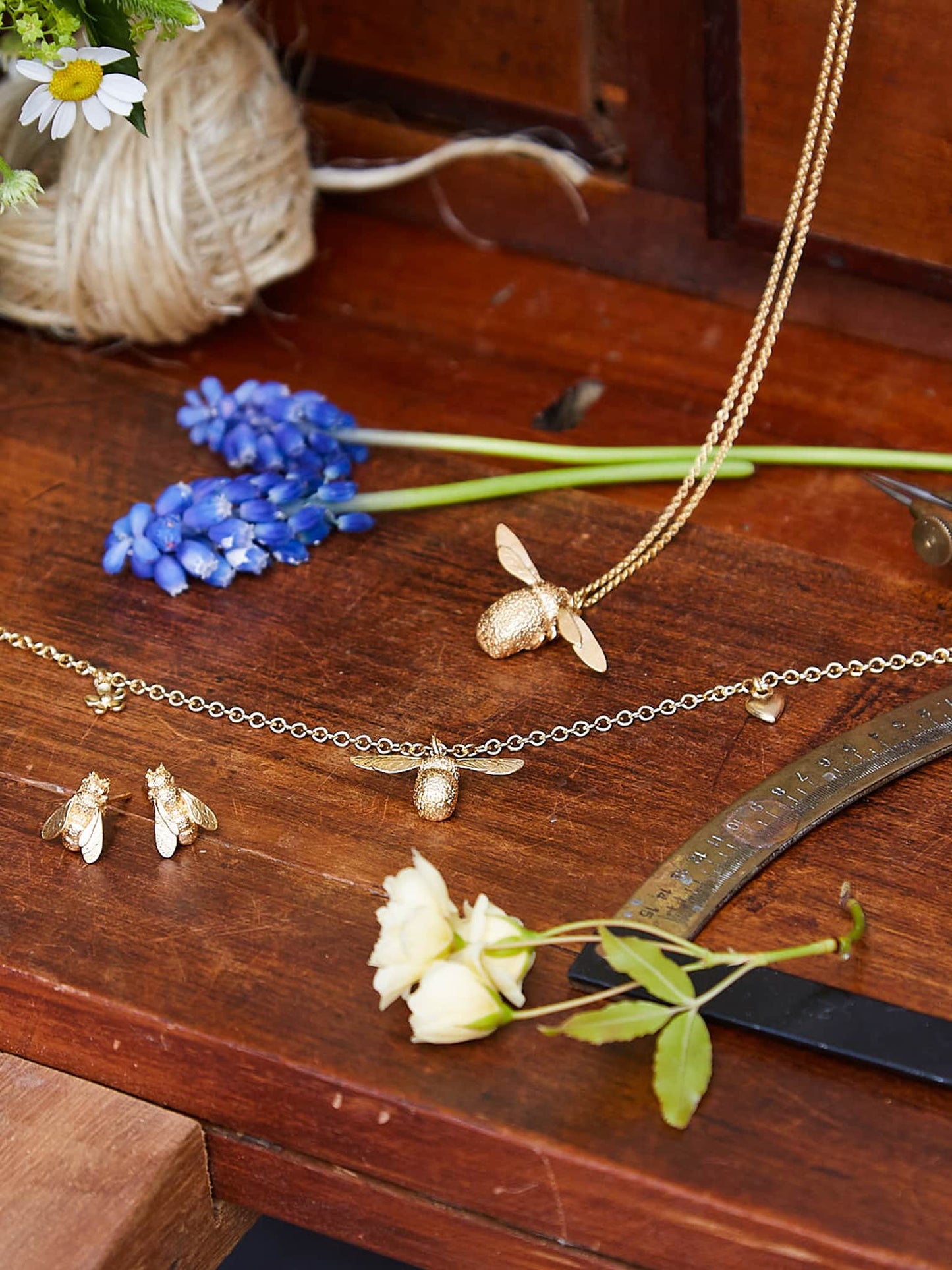 Gold bee-themed jewelry on a wooden surface with flowers