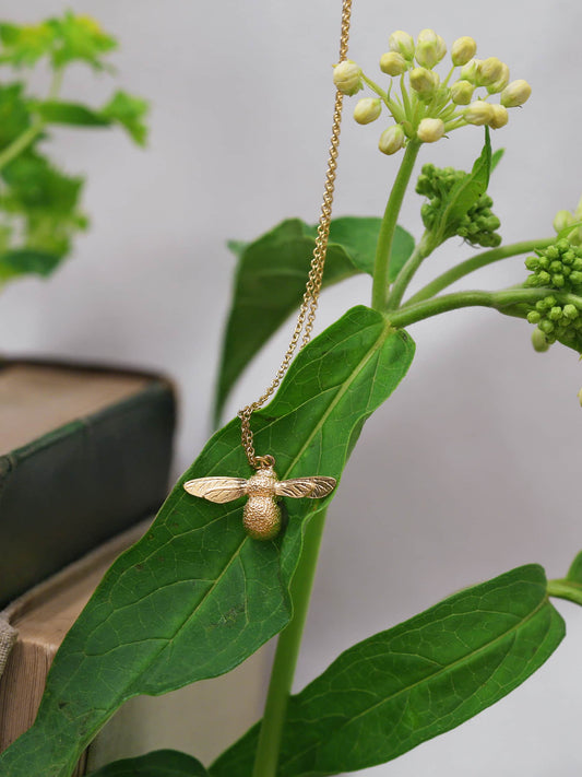 Gold bee necklace hanging on a green leaf