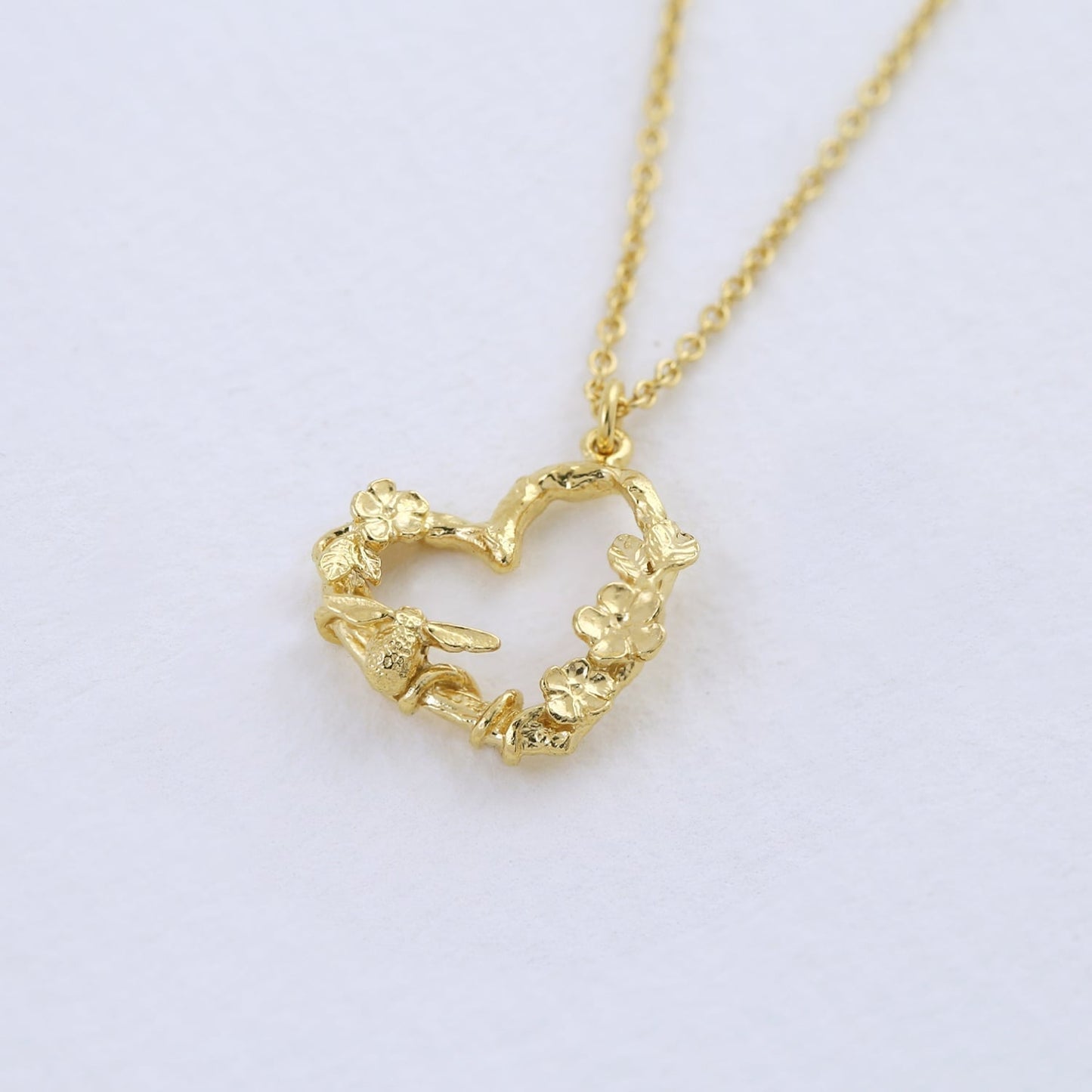 22 carat Yellow Gold Floral Heart Necklace with Itsy Bitsy Bee on a light purple background