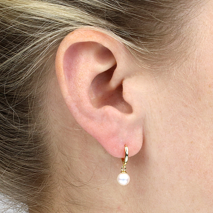 Close-up of an ear wearing a gold earring with a pearl drop.