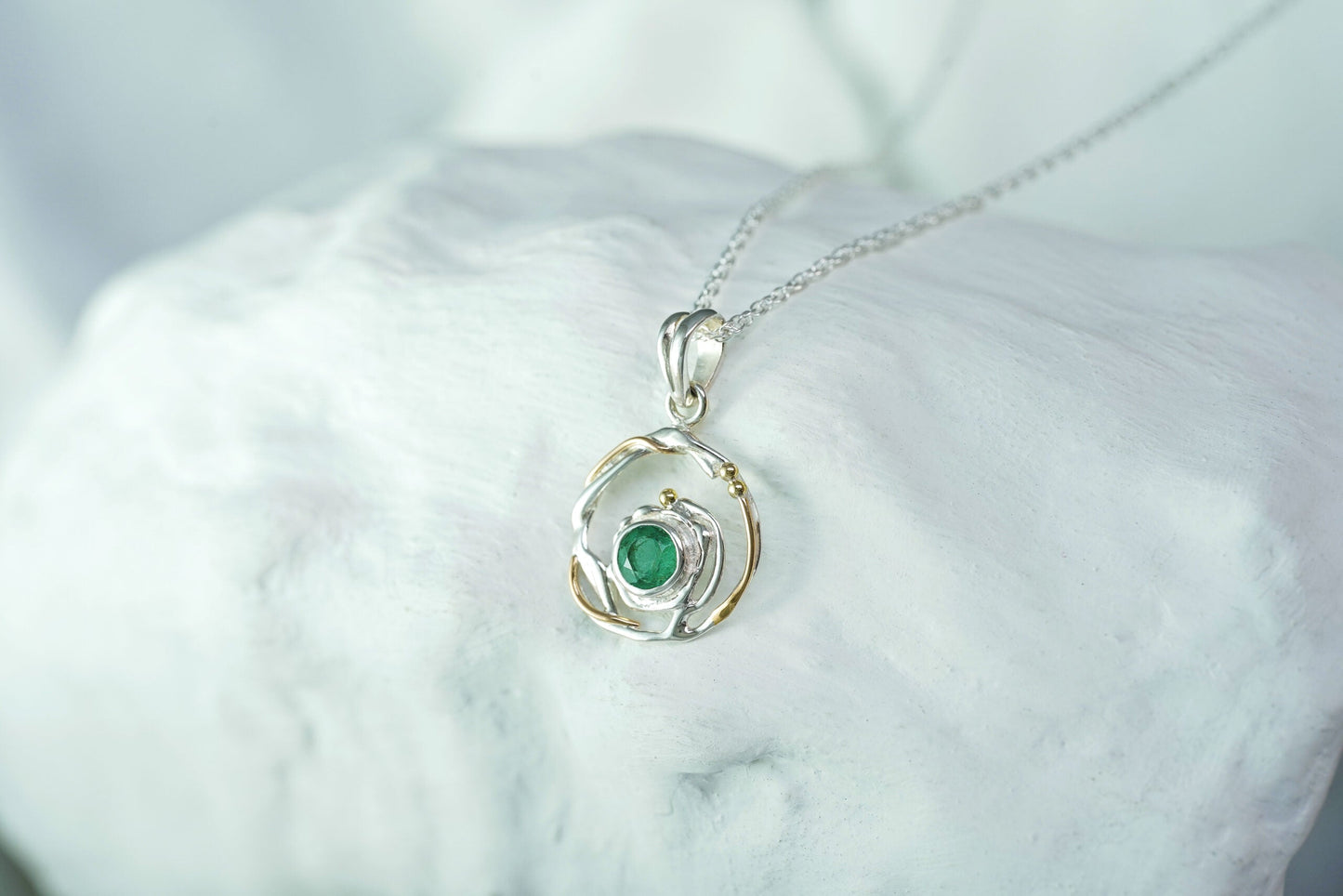 Silver pendant with a green gemstone on a white marble surface