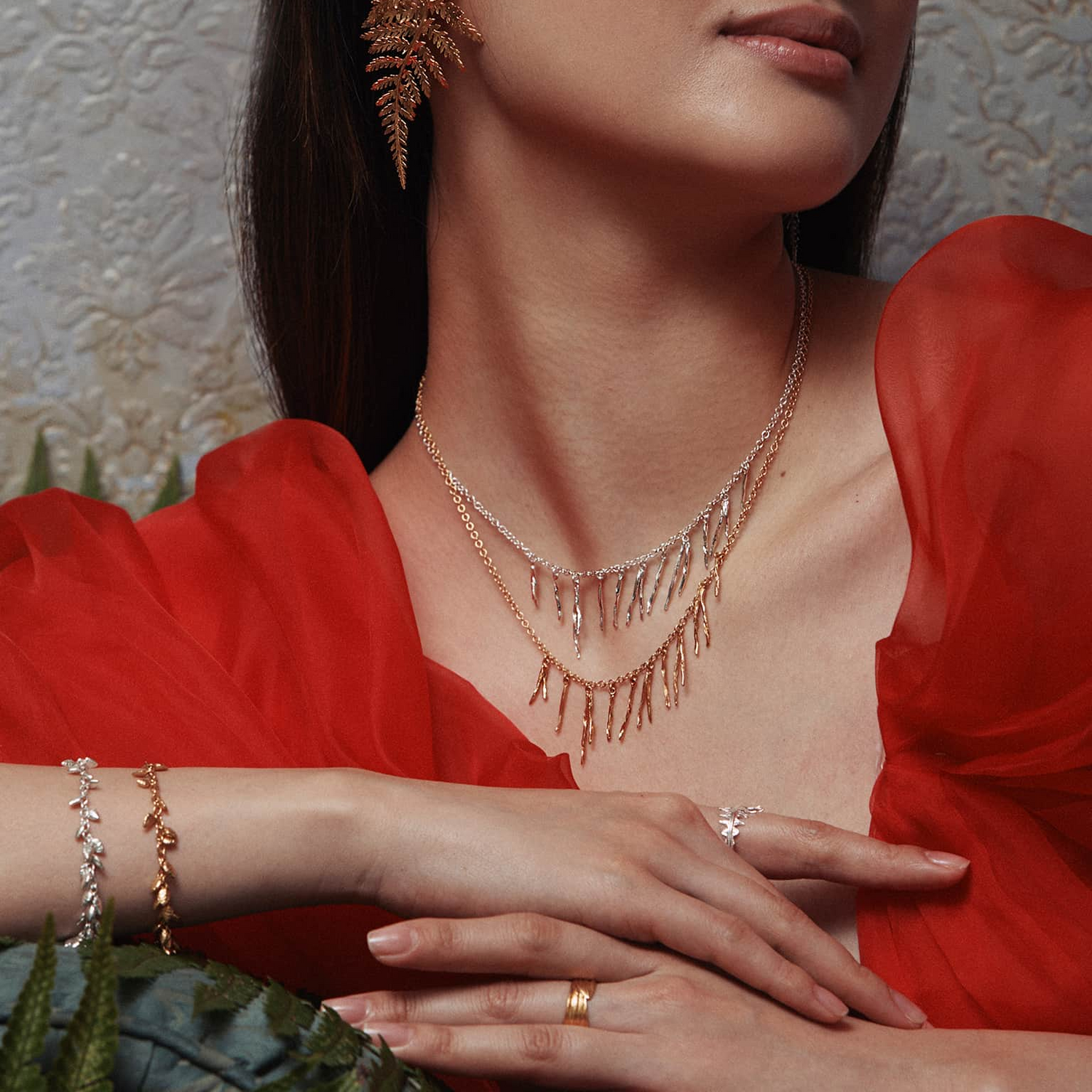 A model's face with their hand touching their hair wearing Alex Monroe earrings and rings