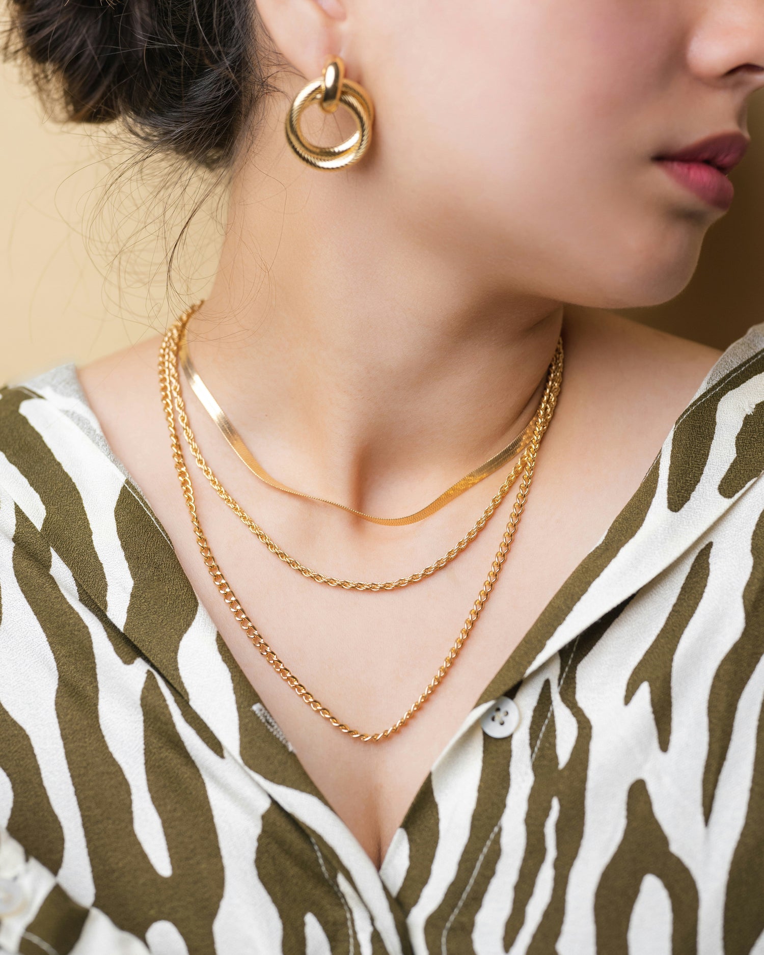 a model wearing three different gold necklaces