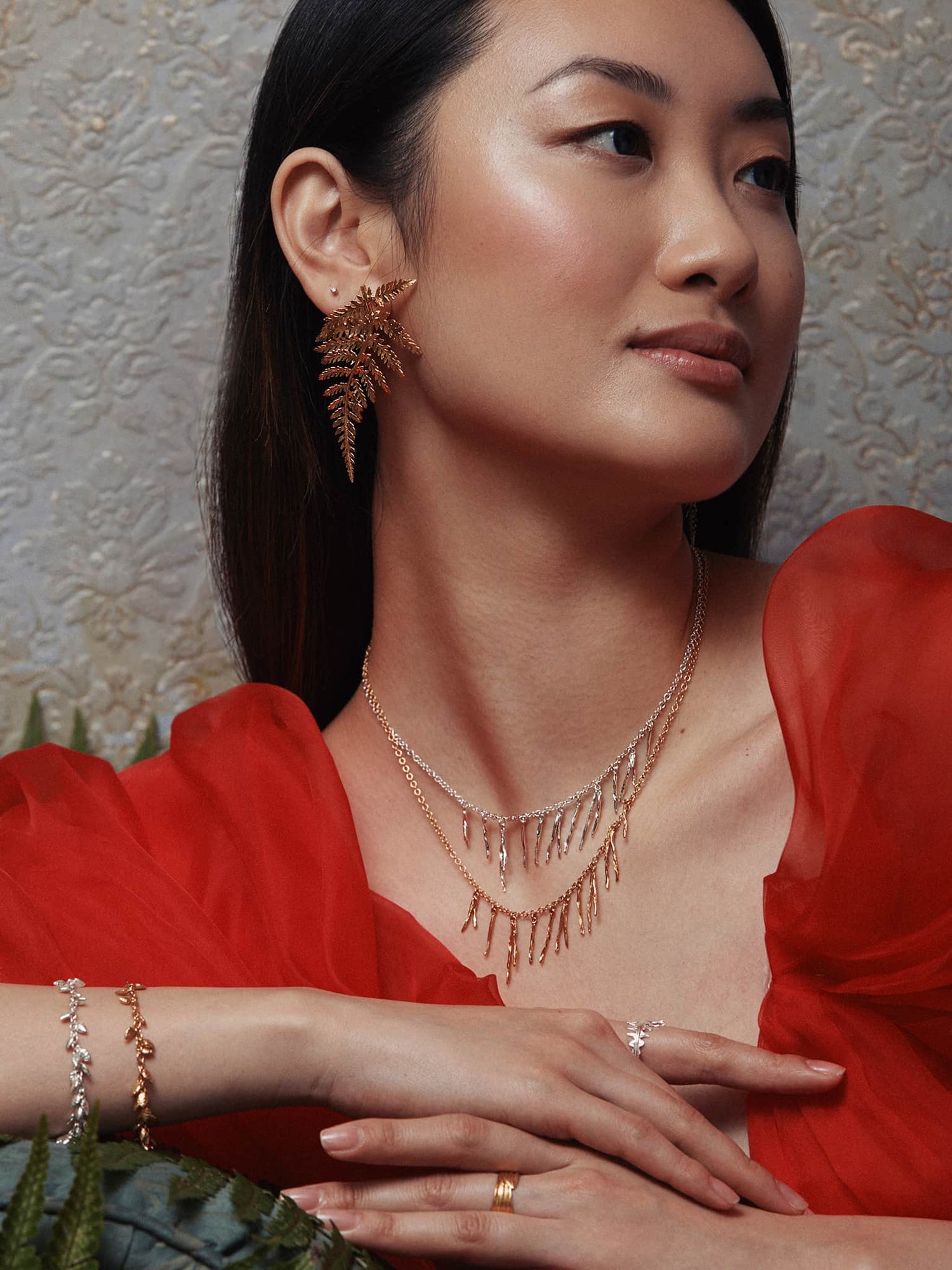 A model's face with their hand touching their hair wearing Alex Monroe earrings and rings