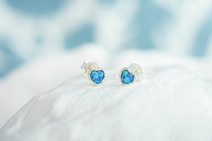 Small Sterling Silver Opalite Heart Studs on a white surface with a blurred blue background