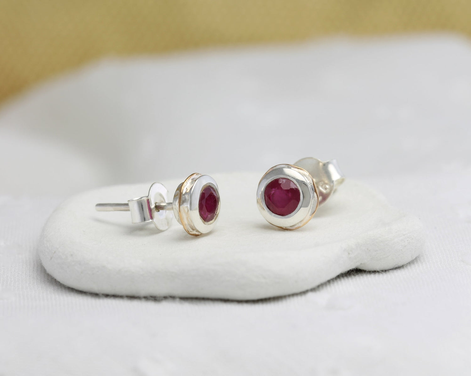 Sterling Silver Ruby & 14 carat Gold Detail Studs on a white cushion