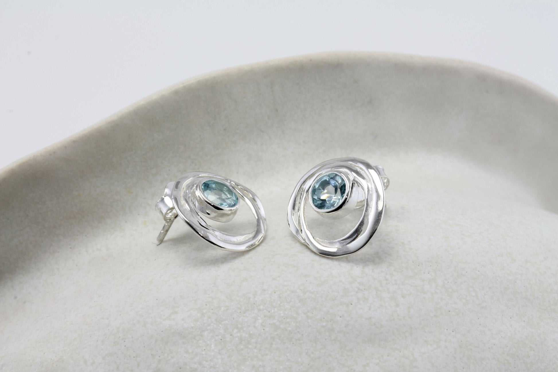 Sterling Silver Blue Topaz Loop Studs on a light gray surface