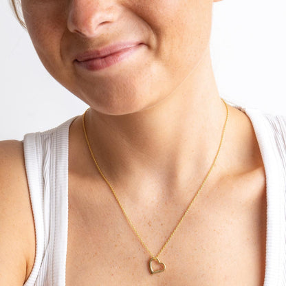 Woman wearing a gold necklace with a heart pendant on a white background