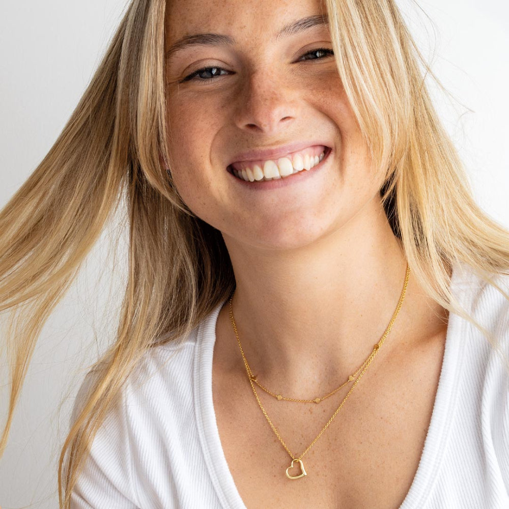 Woman wearing a gold necklace with a heart pendant on a plain background