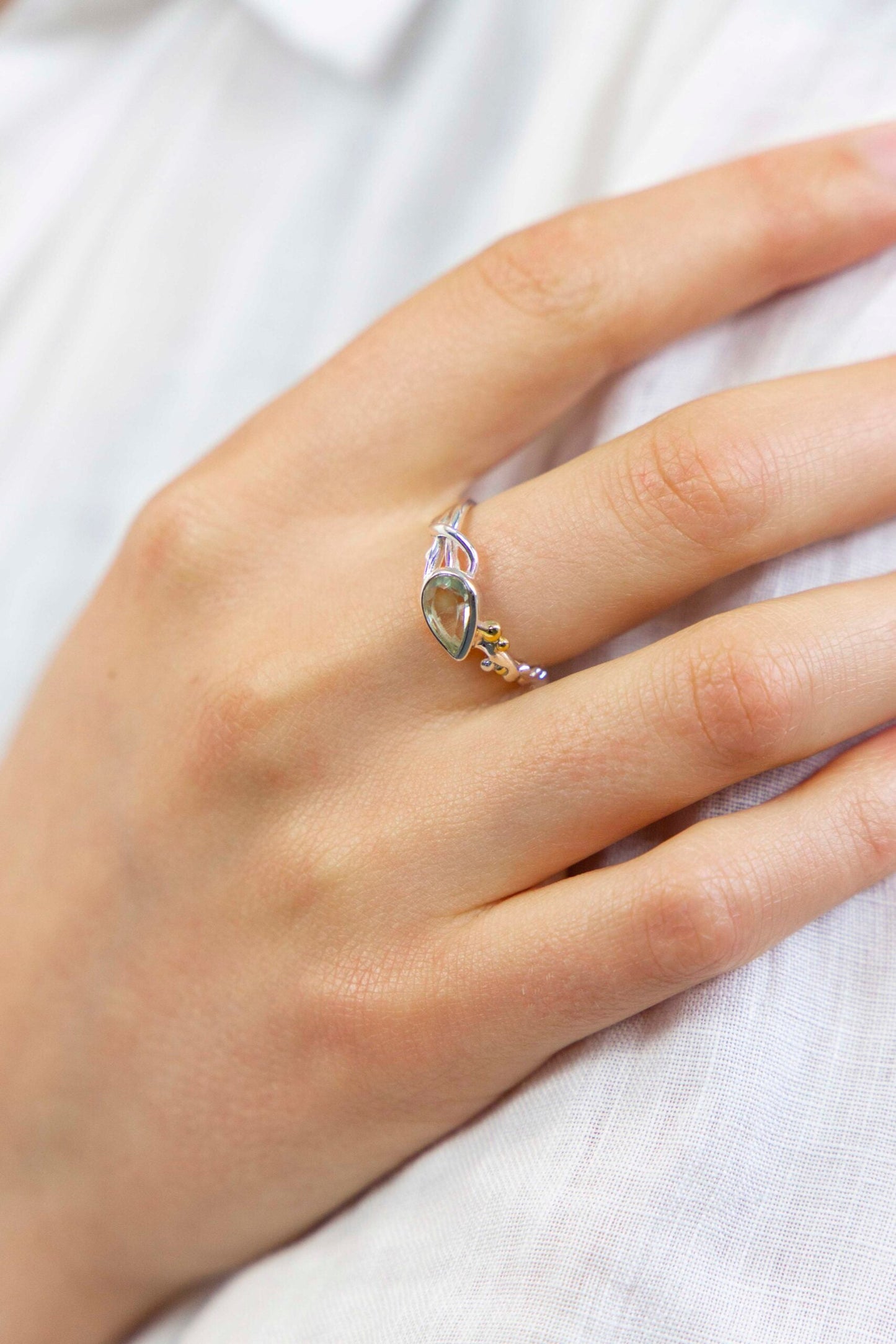 Hand wearing a silver ring with a green gemstone on a white background