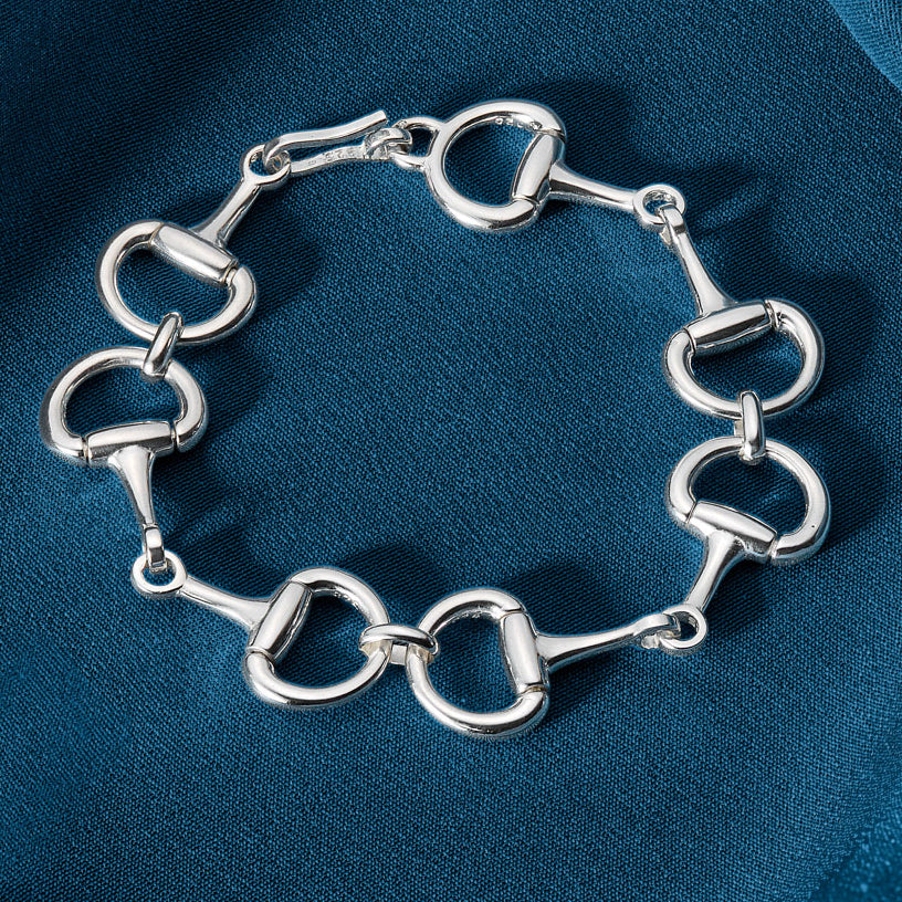 Silver bracelet with horse bit links on a blue fabric background