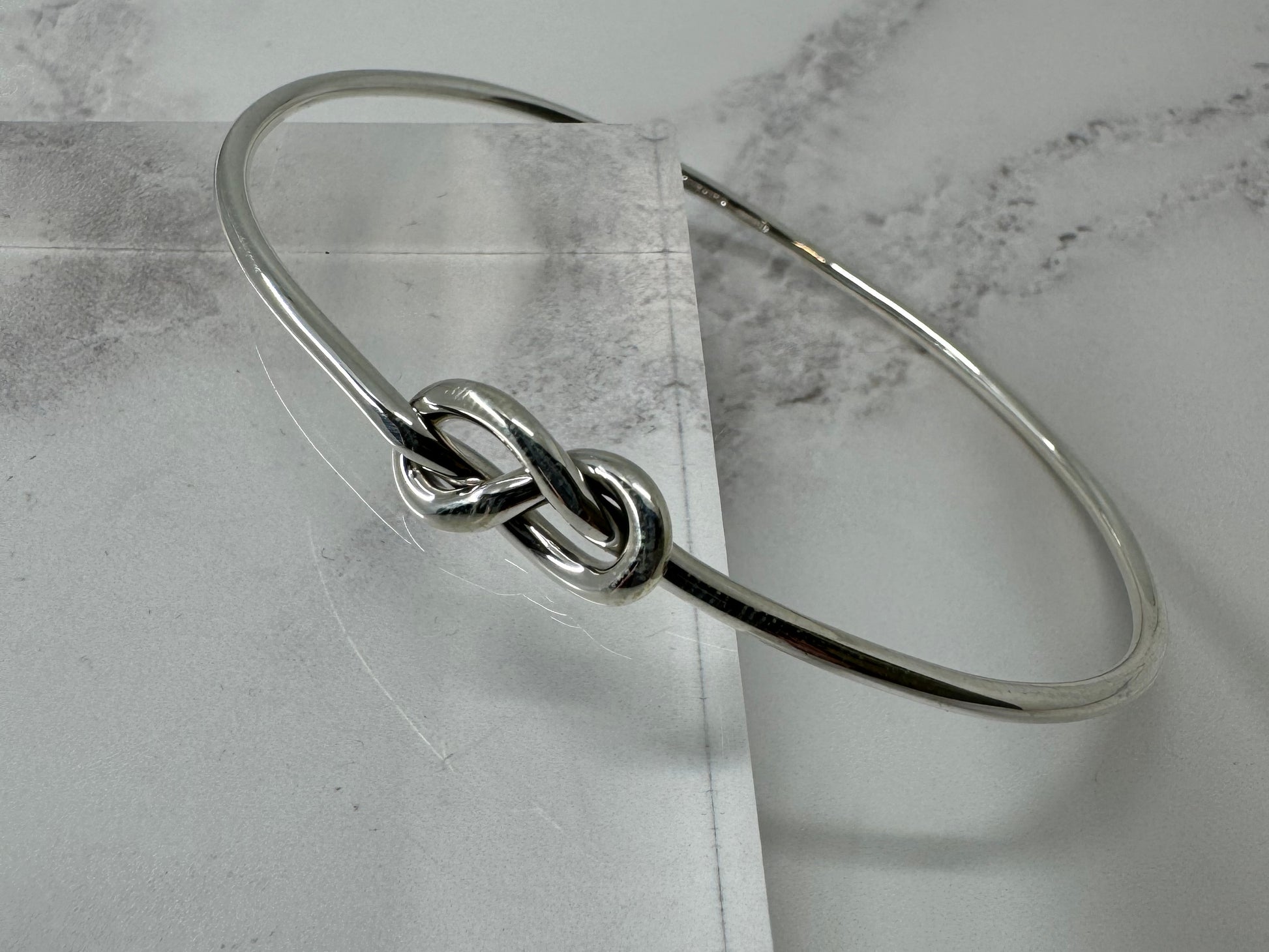 Silver bracelet with a knot design on a marble surface