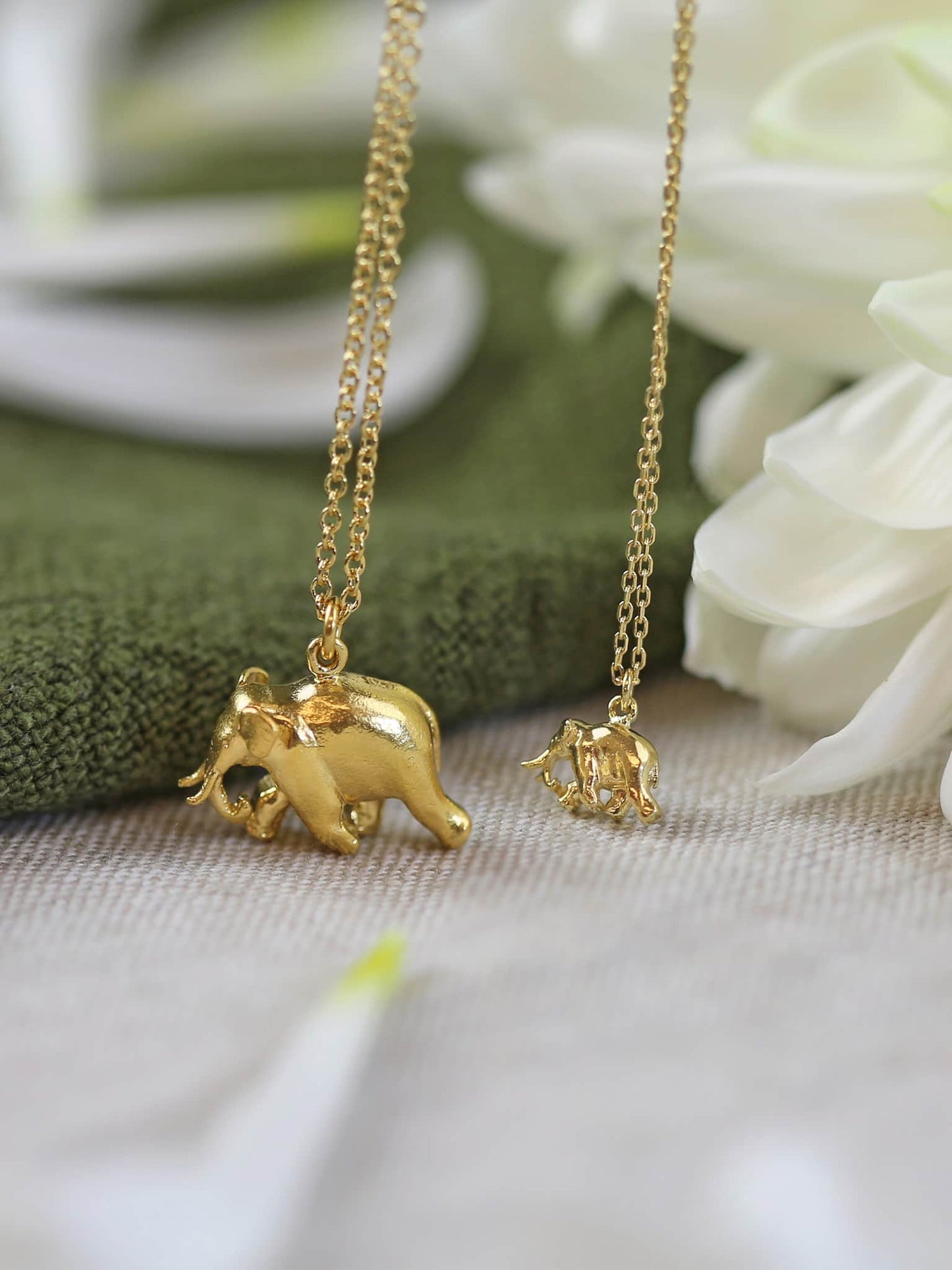 Gold elephant pendant necklaces on a chain with a soft focus background