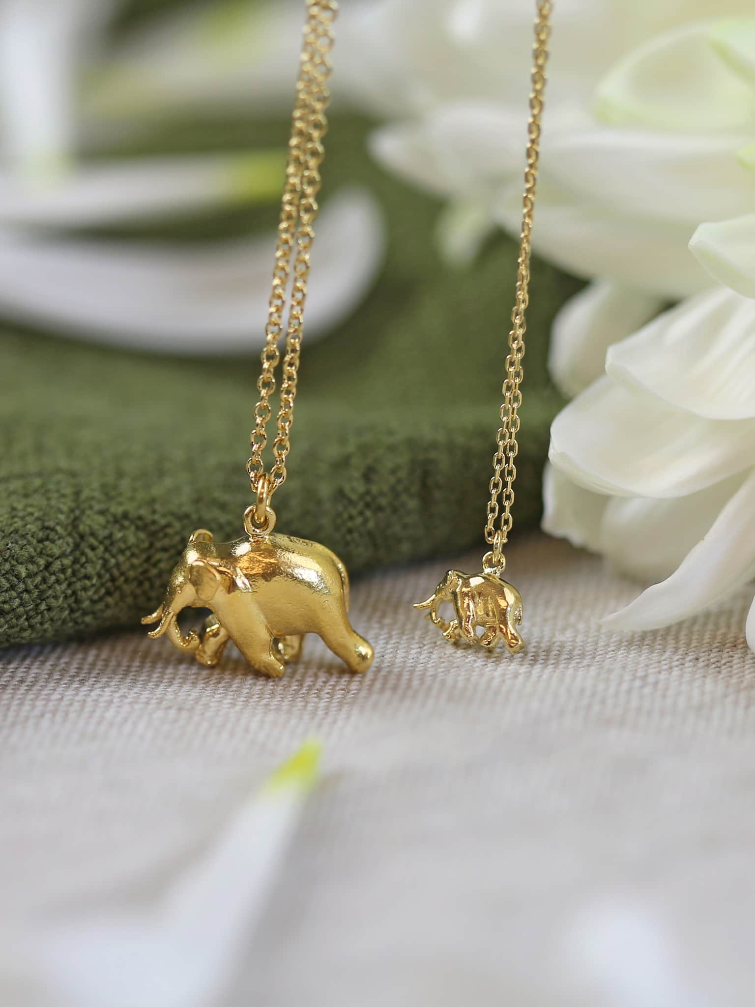 Gold elephant pendant necklaces on a chain with a soft focus background