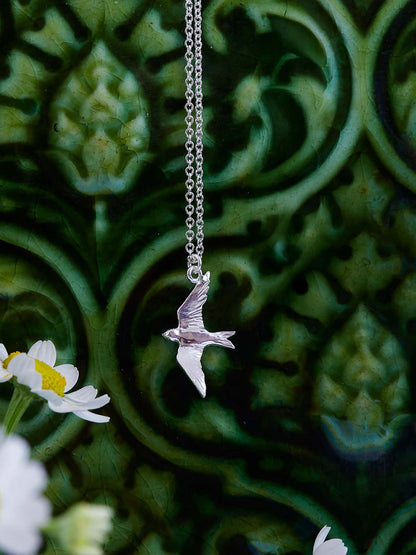 Alex Monroe Sterling Silver Flying Swallow Necklace against a green floral background
