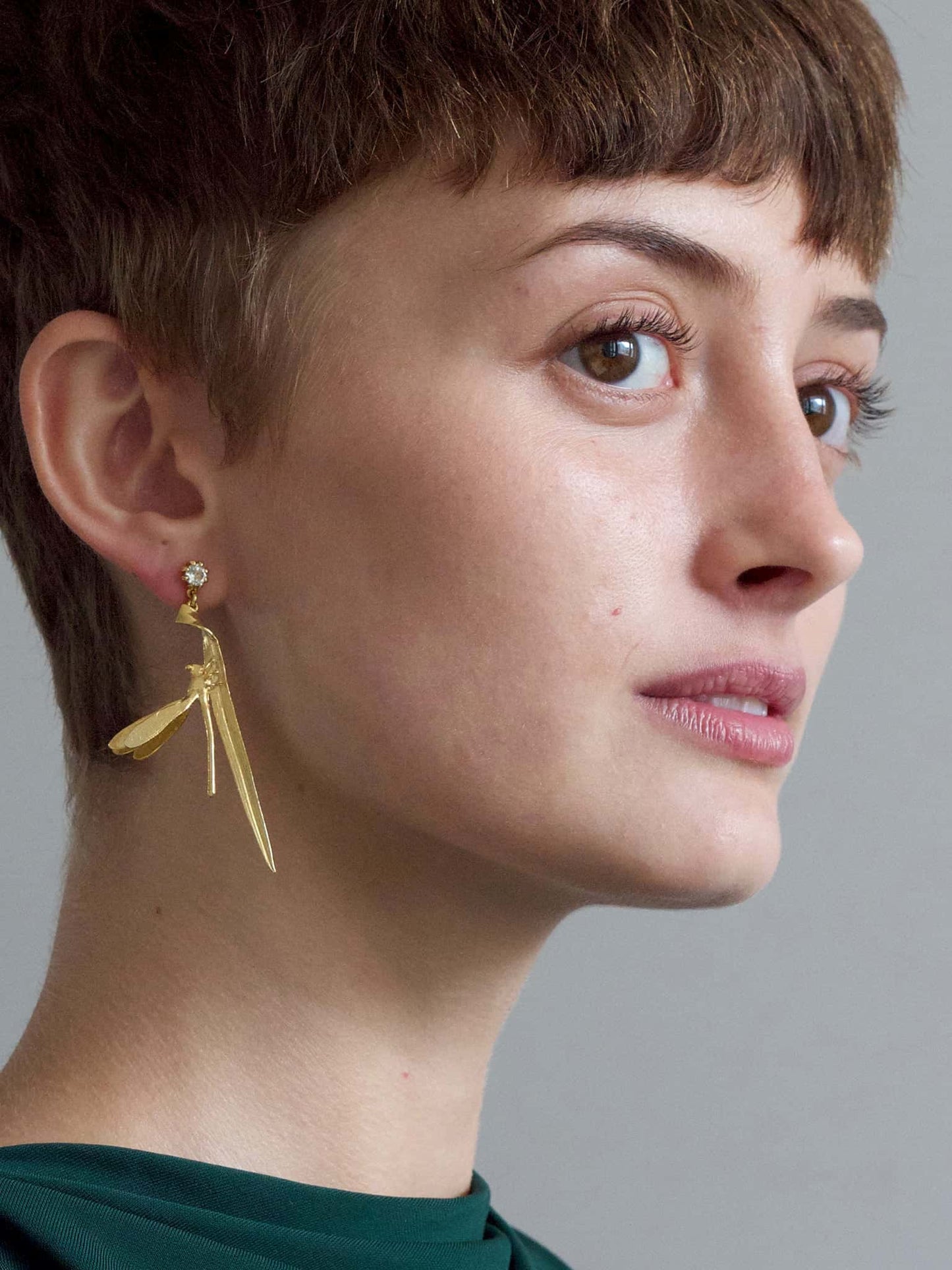 A model wearing an Alex Monroe Statement 18carat Vermeil Damsel Fly & Grassblade Green Amethyst Drop Earring