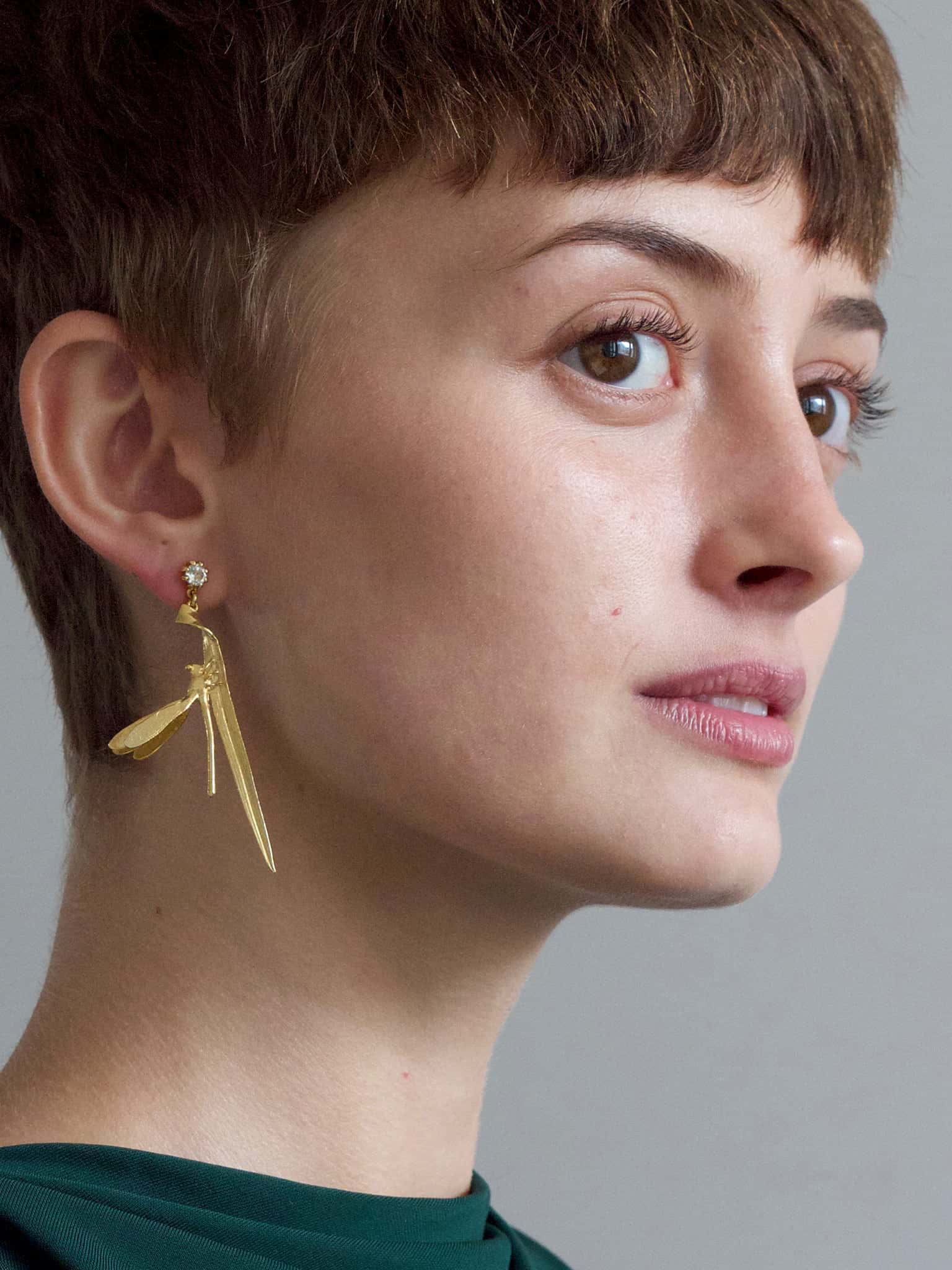 A model wearing an Alex Monroe Statement 18carat Vermeil Damsel Fly & Grassblade Green Amethyst Drop Earring