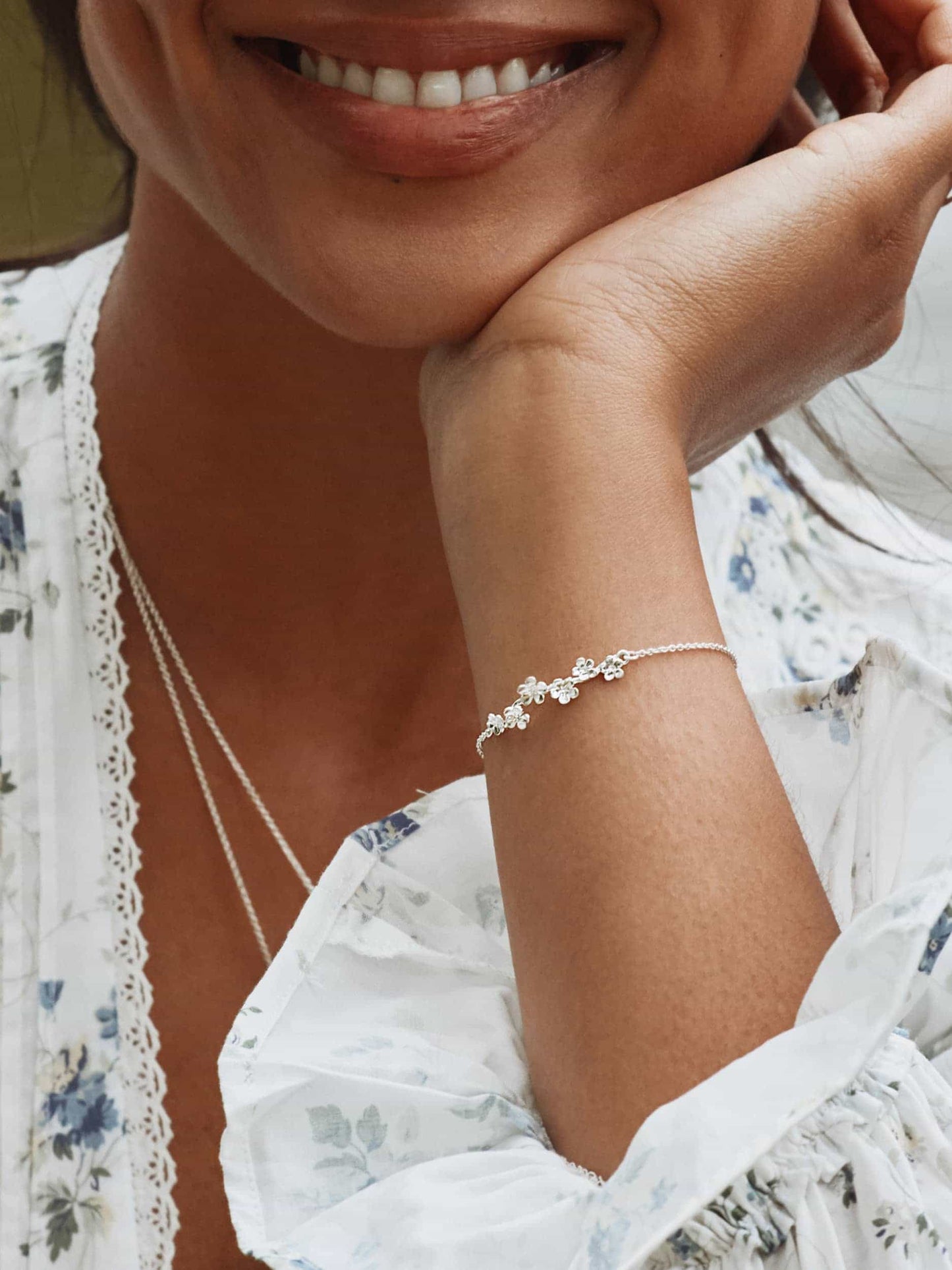 Close-up of a woman wearing a silver bracelet and necklace, with a blurred background.
