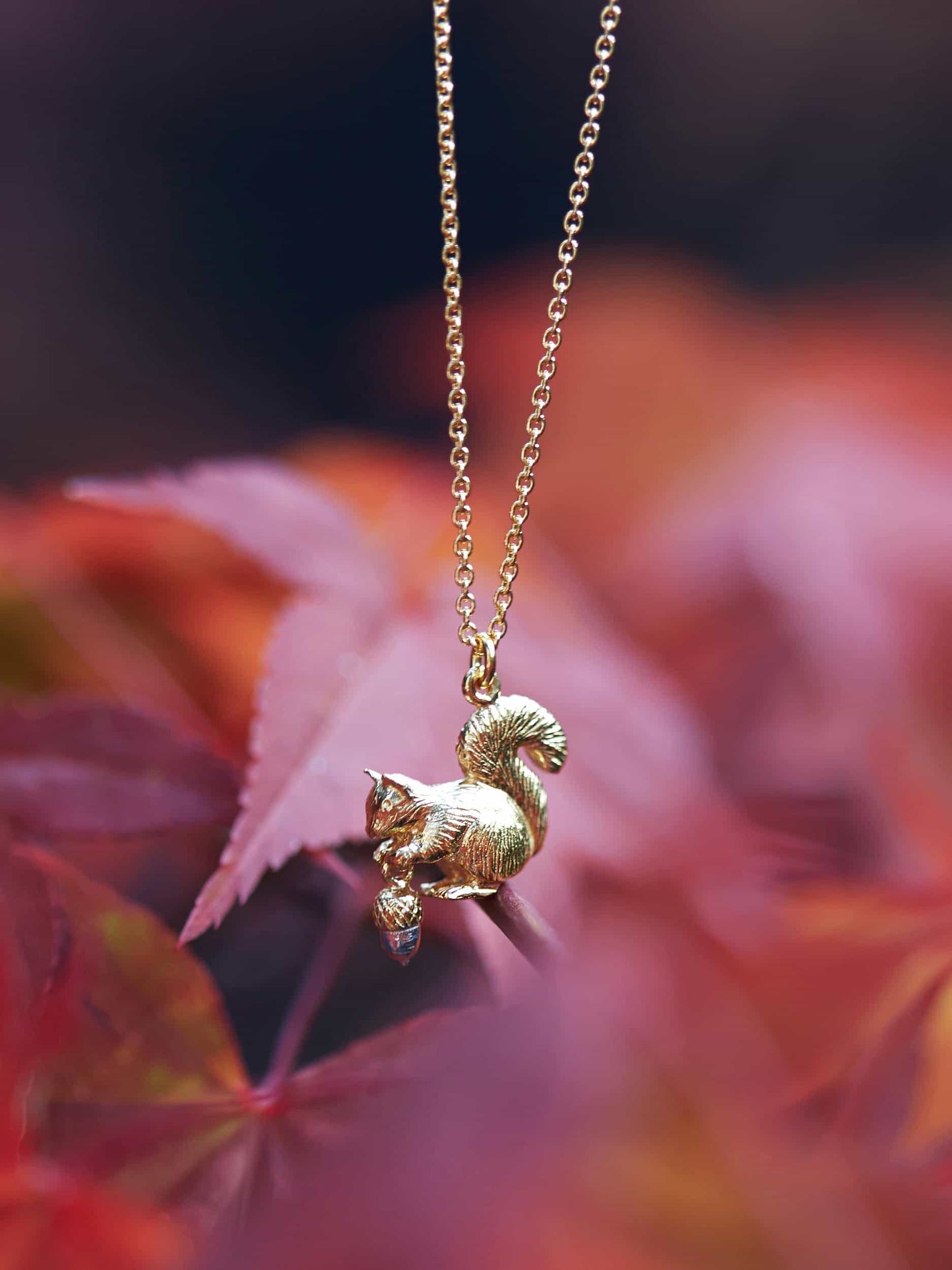Alex Monroe 22 carat Gold Vermeil & Sterling Silver Squirrel & Acorn Necklace on a chain with a blurred autumn leaf background