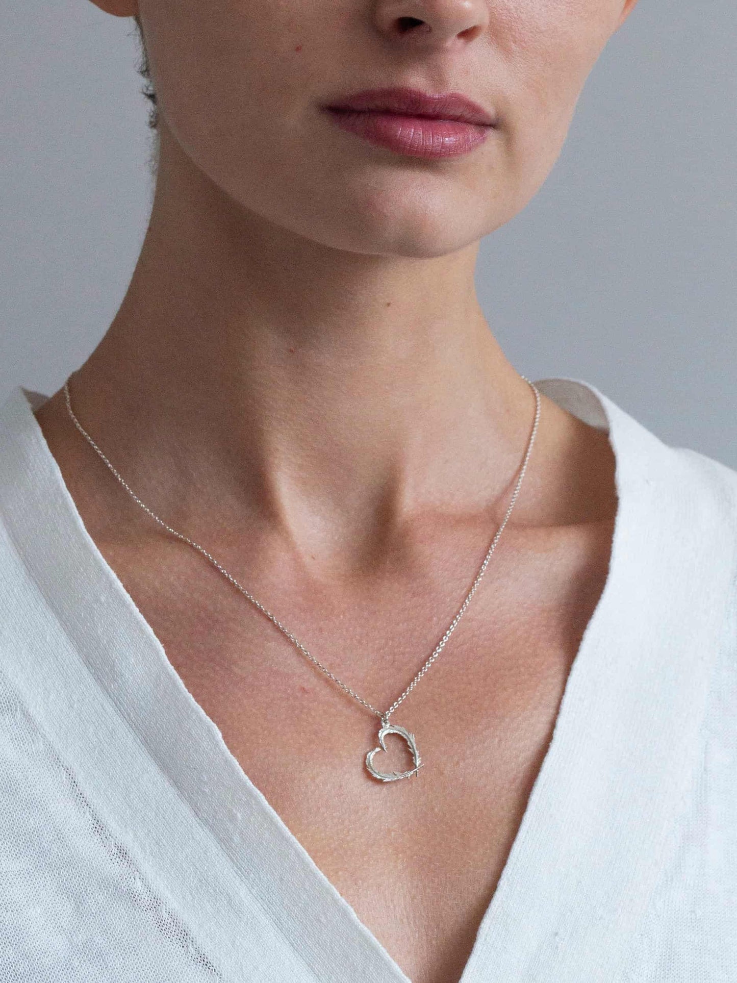 Close-up of a person wearing a silver heart-shaped necklace against a neutral background