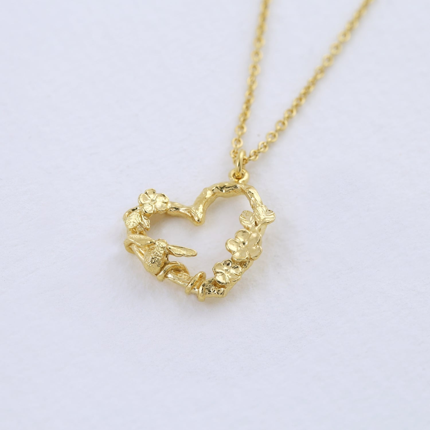 22 carat Yellow Gold Floral Heart Necklace with Itsy Bitsy Bee on a light purple background