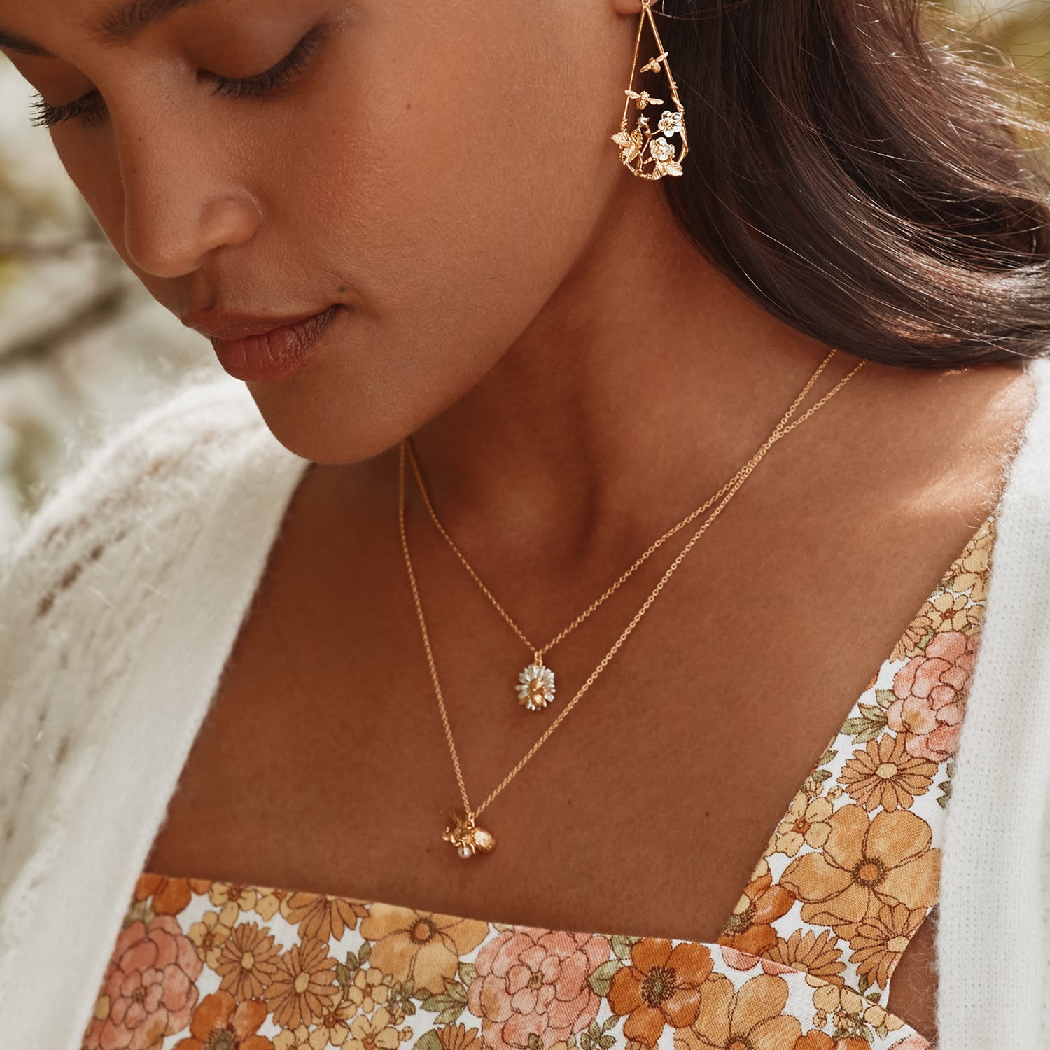 Woman wearing a floral dress and Alex Monroe Mixed Silver & Gold Plate Daisy Necklace with Teeny Weeny Bee with a blurred natural background