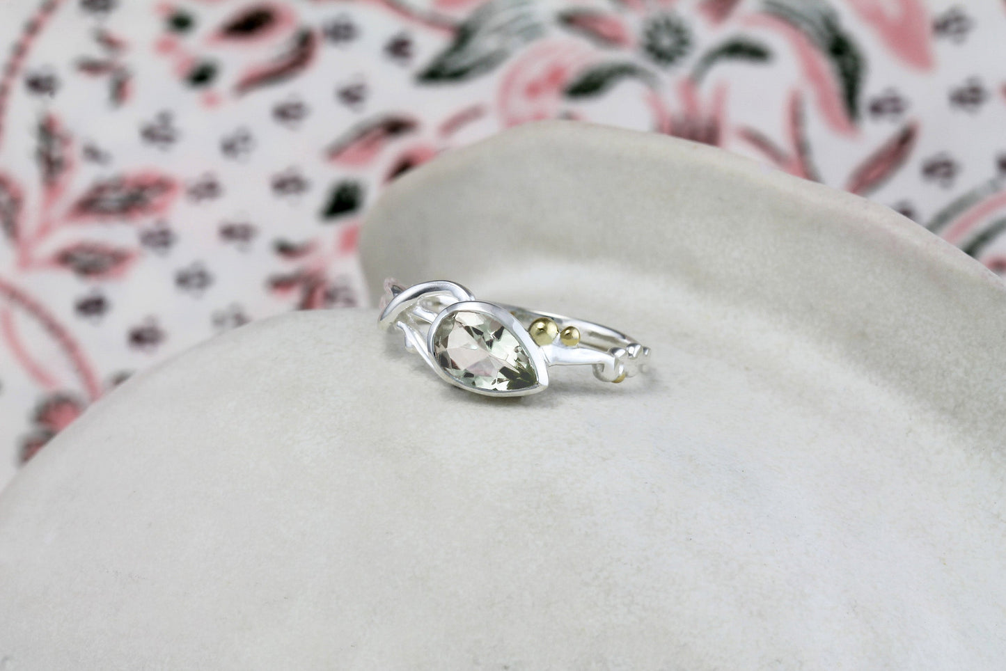 Silver ring with a gemstone on a white cushion with a floral-patterned fabric background