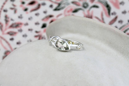 Silver ring with a gemstone on a white cushion with a floral-patterned fabric background