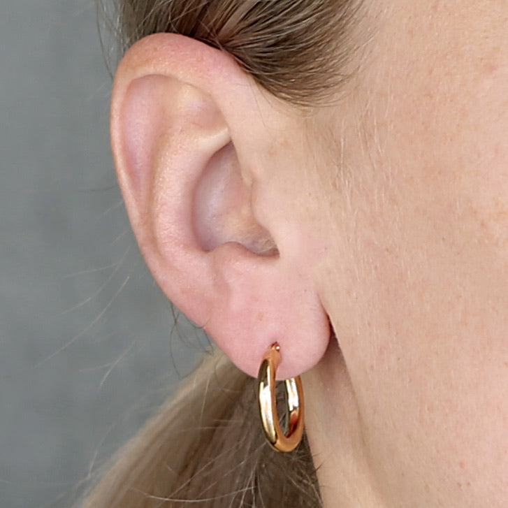 Close-up of an ear wearing a gold hoop earring with a neutral background