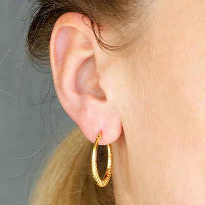 Close-up of an ear wearing a gold hoop earring with a neutral background