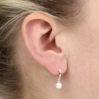 Close-up of an ear wearing a silver hoop earring with a pearl pendant.