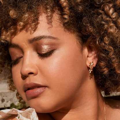 Close-up of a woman with curly hair wearing earrings, with a blurred natural background