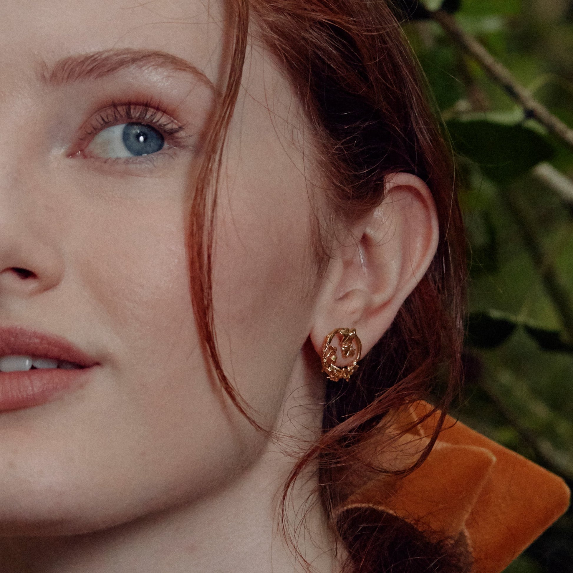 Close-up of a woman wearing a gold earring with a blurred green background
