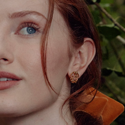 Close-up of a woman wearing a gold earring with a blurred green background