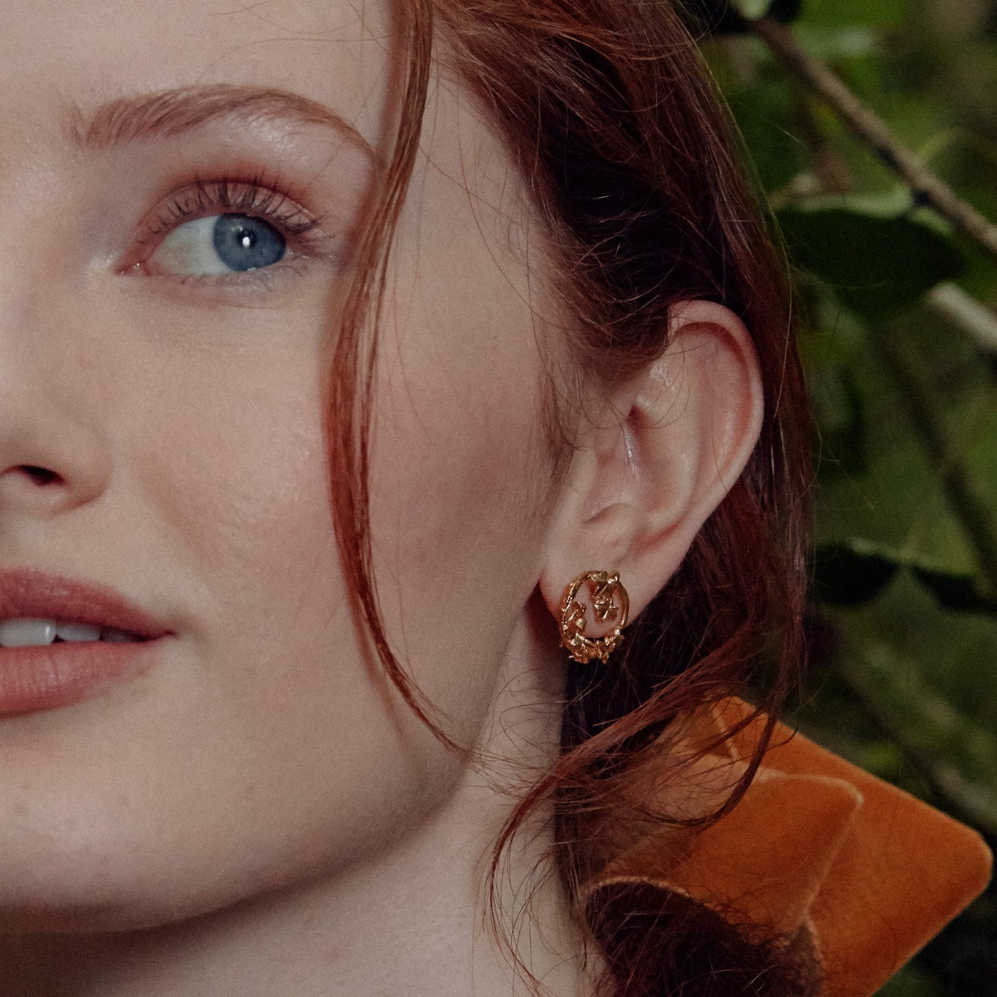 Close-up of a woman wearing a gold Vermeil Woodland Loop Stud Earring with a blurred green background