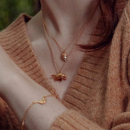 Close-up of a person wearing an Alex Monroe 22 carat Yellow Gold Vermeil Foraging Badger necklace and bracelet with a soft brown background