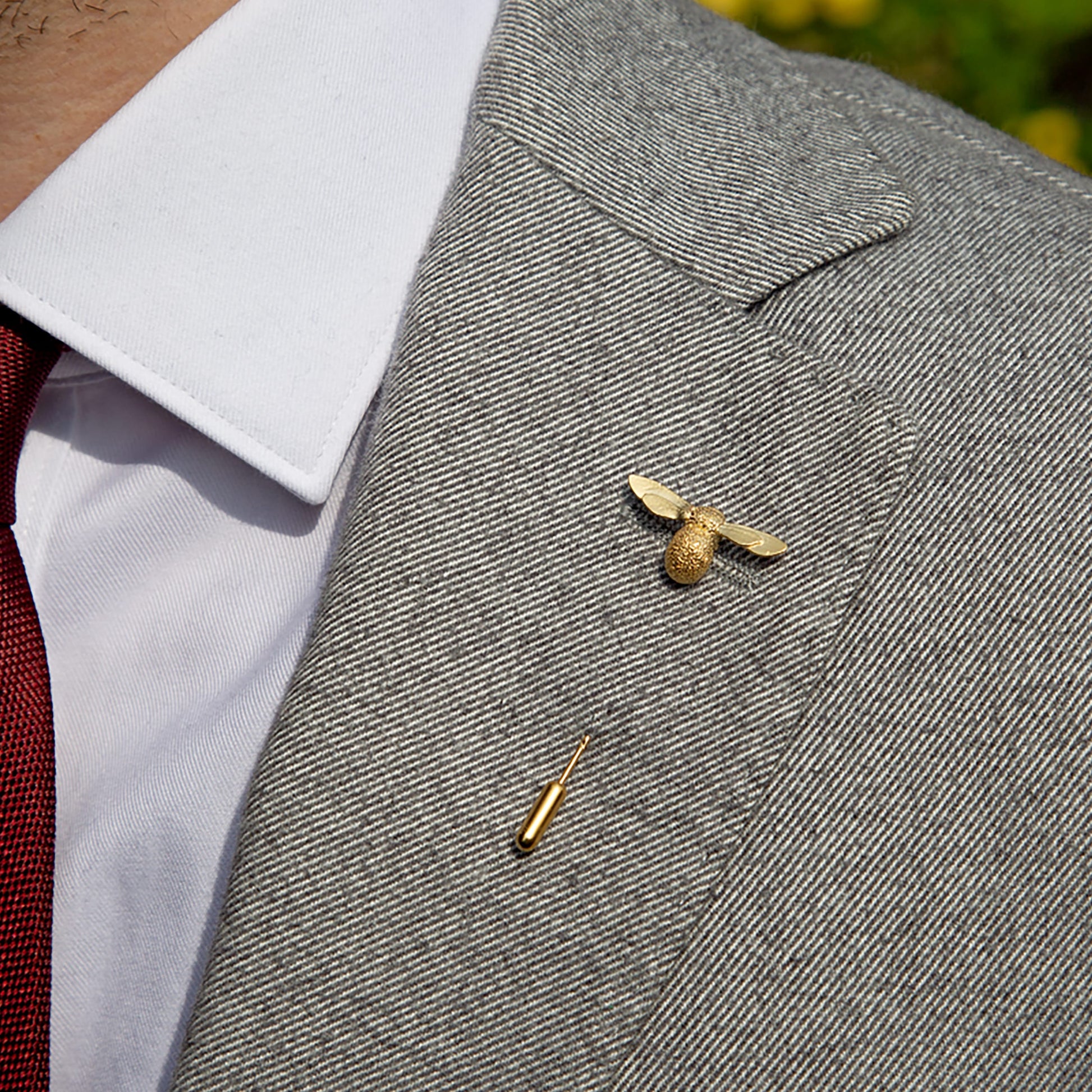 Gold bee lapel pin on a gray suit jacket with a blurred background