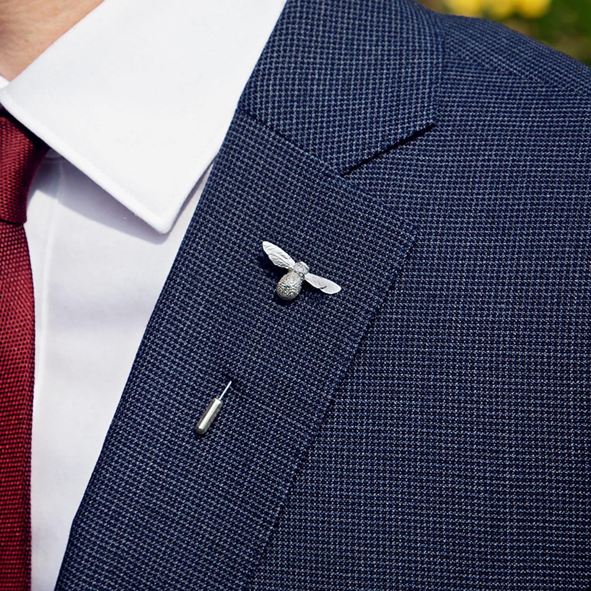 Navy blazer with a silver bee pin on a blurred outdoor background
