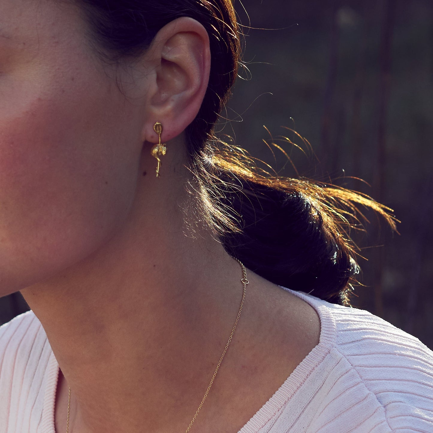 Close-up of a person wearing gold earrings and a necklace with a blurred background