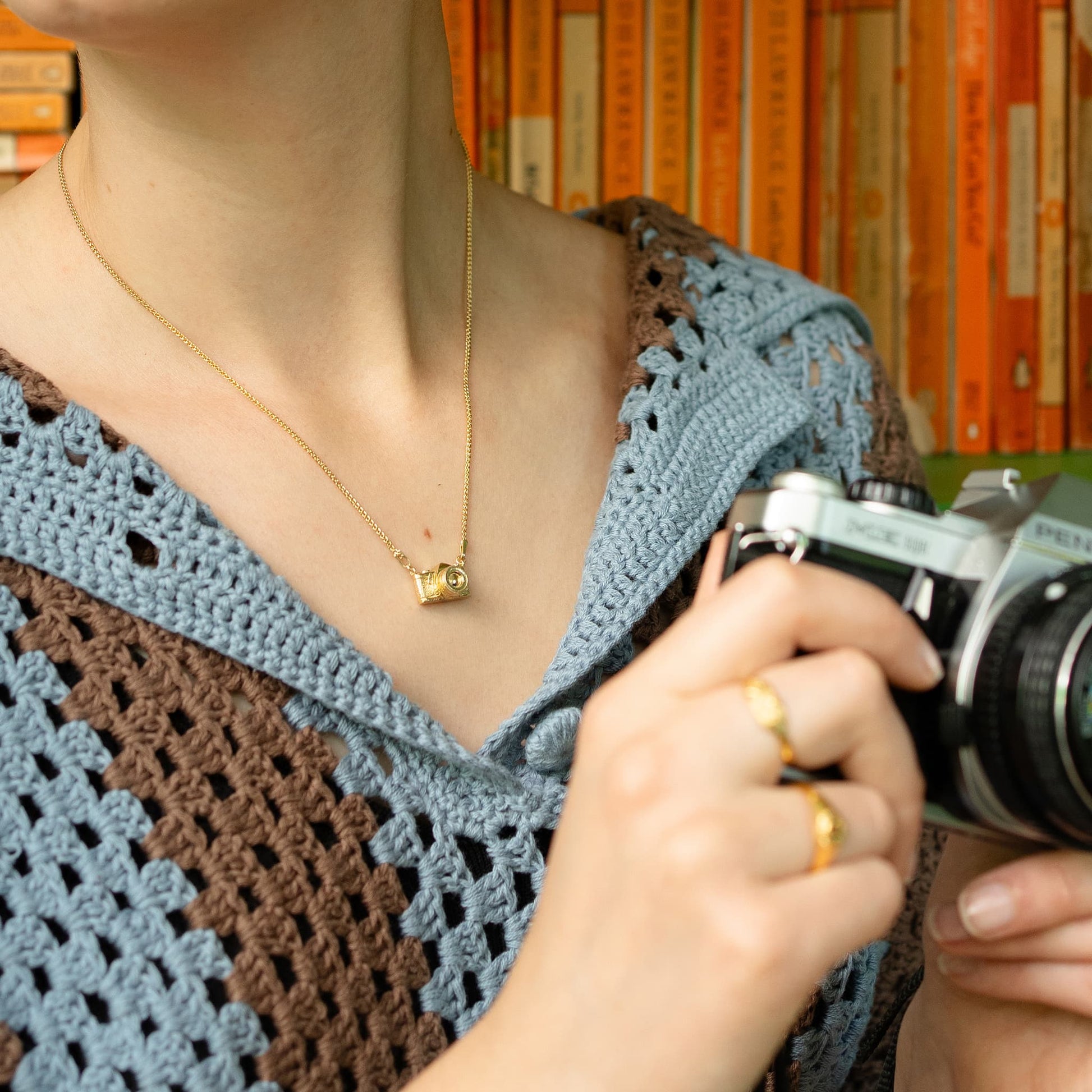 Alex Monroe gold In-line Vintage Camera Necklace worn by a model holding a camera