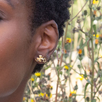 Close-up of a person's ear with a Alex Monroe 22 carat Yellow Gold Vermeil Lucky Clover Stud Earring against a natural background