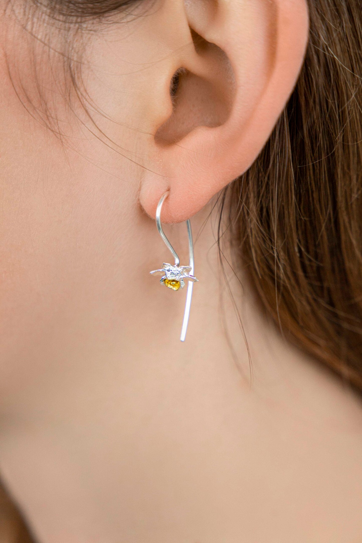 Close-up of a person wearing a silver earring with a yellow gemstone.