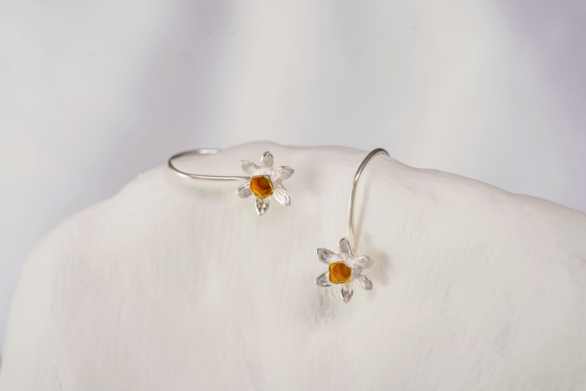 Silver earrings with orange stones on a white mannequin bust against a light gray background