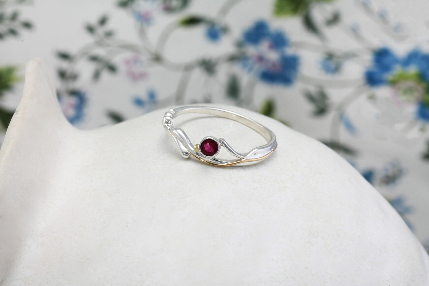 Silver ring with a red gemstone on a white surface with a floral background