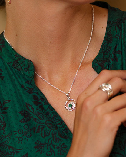 Person wearing a silver necklace with a green pendant and a ring on a blurred background