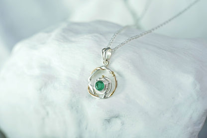 Silver pendant with a green gemstone on a white marble surface
