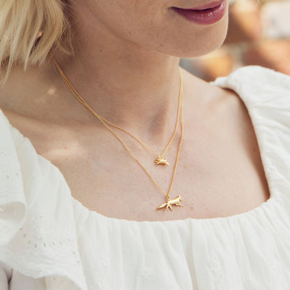 Close-up of a person wearing two gold necklaces with small pendants.
