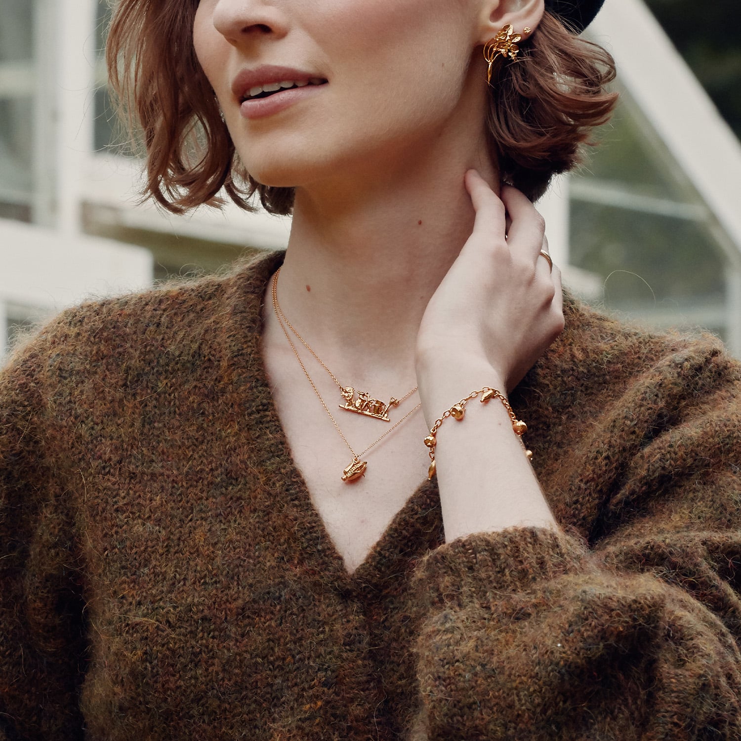 A woman wearing Alex Monroe gold Inline Allotment Necklace and charm bracelet